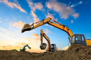 Three excavators work on construction site at sunset